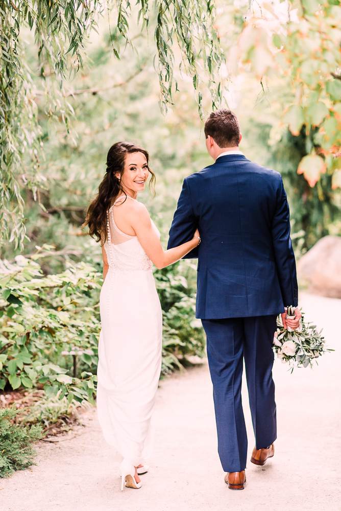 bride and groom holding hands walking away from camera bridge looking over shoulder smiling at camera at Fredrick Meijer Gardens wedding by Stephanie Anne Photography