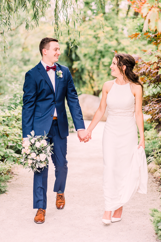 Bride and groom stop on path smiling at each other holding hands at Fredrick Meijer Gardens by Grand Rapids wedding photographer Stephanie Anne