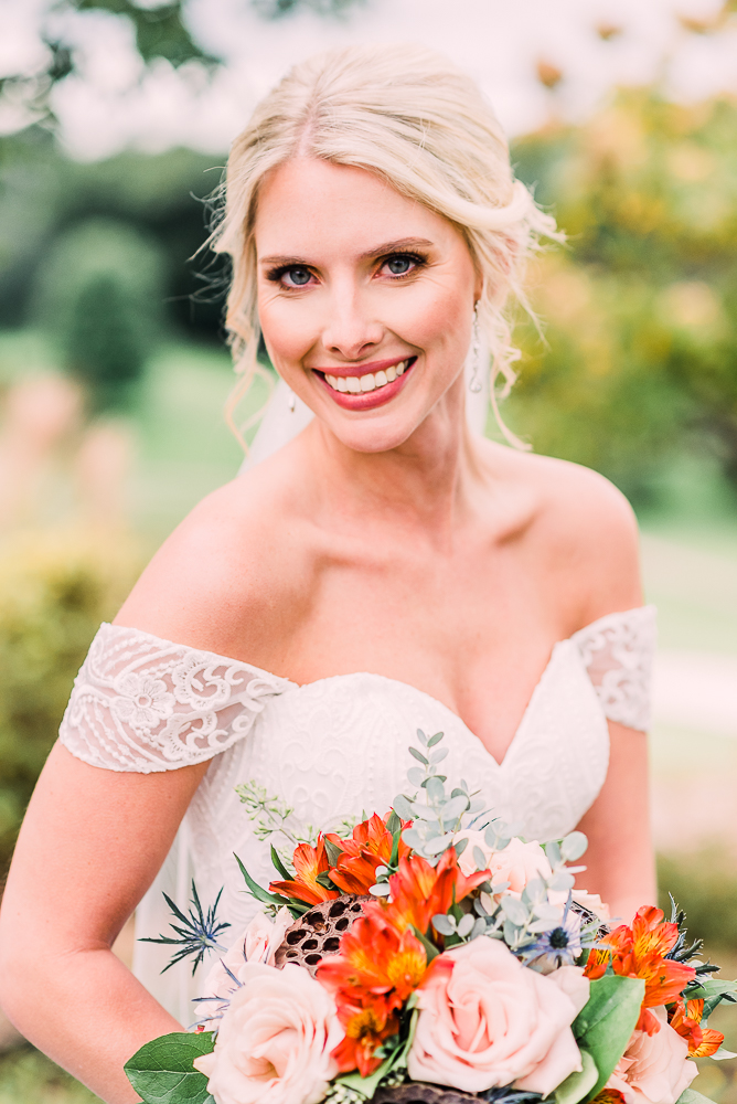 Bride smiling with blonde hair holding orange and soft blue floral bouquet at Kalamazoo Country Club