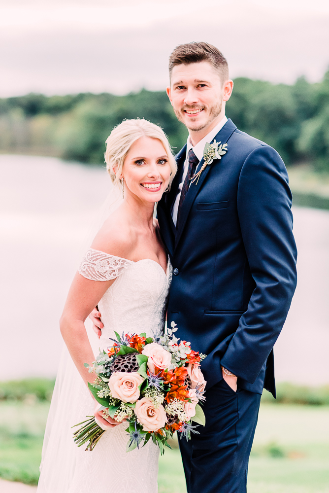 Bride and groom facing each other facing camera smiling holding orange soft  blue and soft pink wedding bouquet at Kalamazoo Country Club