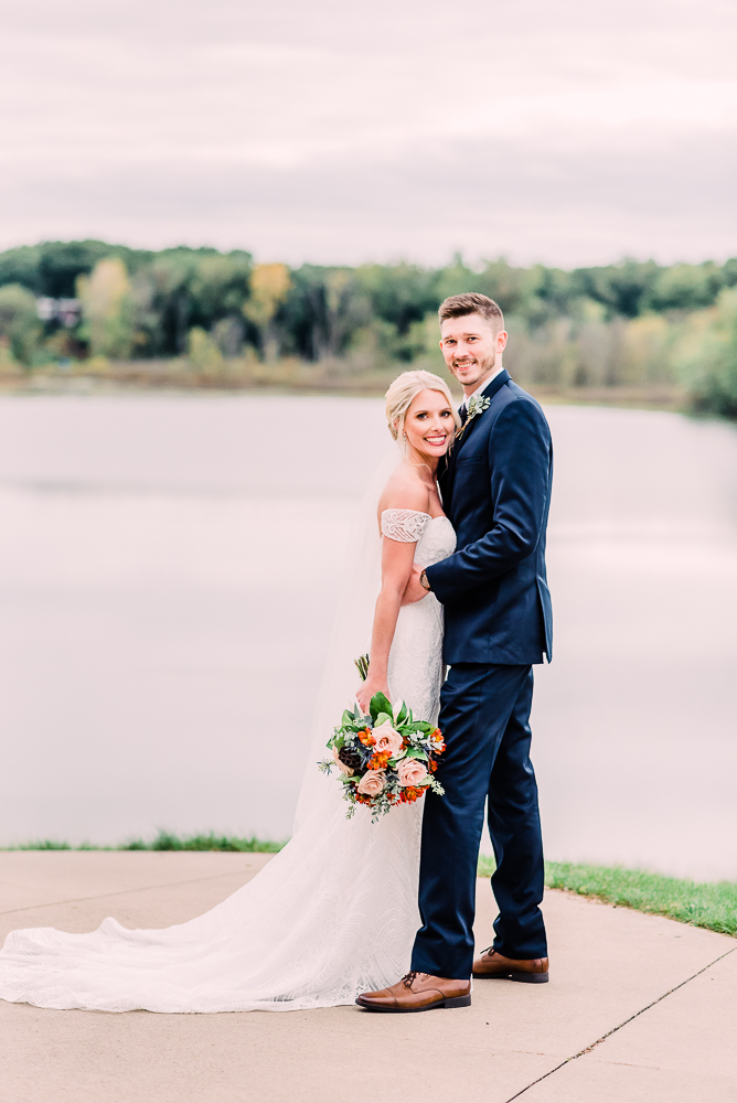 Bride and groom standing facing each other looking at camera smiling holding orange soft blue and pink bouquet at Kalamazoo Country Club Stephanie Anne Photography