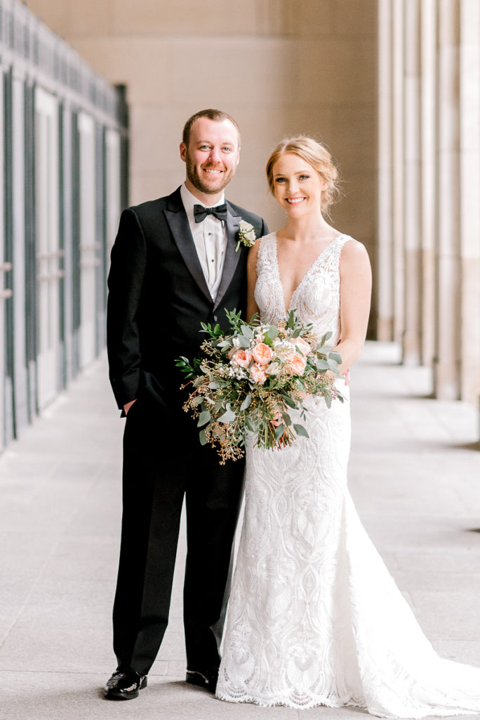 Bride and groom standing between concrete pillars in wedding dress and tuxedo holding bouquet at Civic Center in Grand rapids Michigan by photographer Stephanie Anne