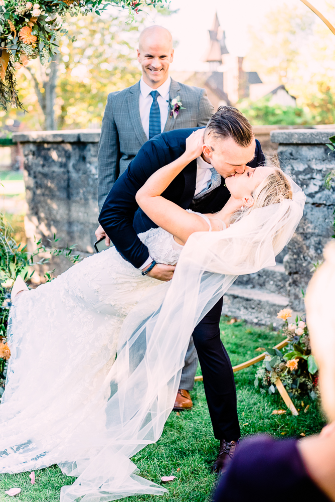 Bride and groom first kiss under circle alter with golden warm hue flowers groom leaning back bride for first kiss by Grand Rapids Wedding photographer Stephanie Anne 