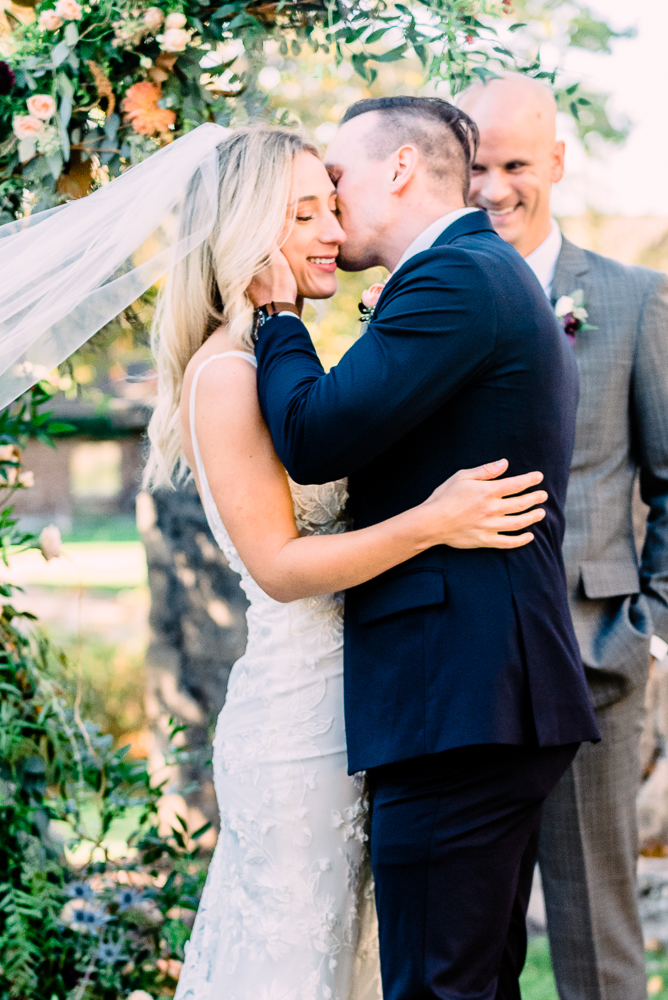 Bride and groom standing at alter groom kissing bride on cheek in navy blue tux by Grand Rapids Wedding photographer Stephanie Anne